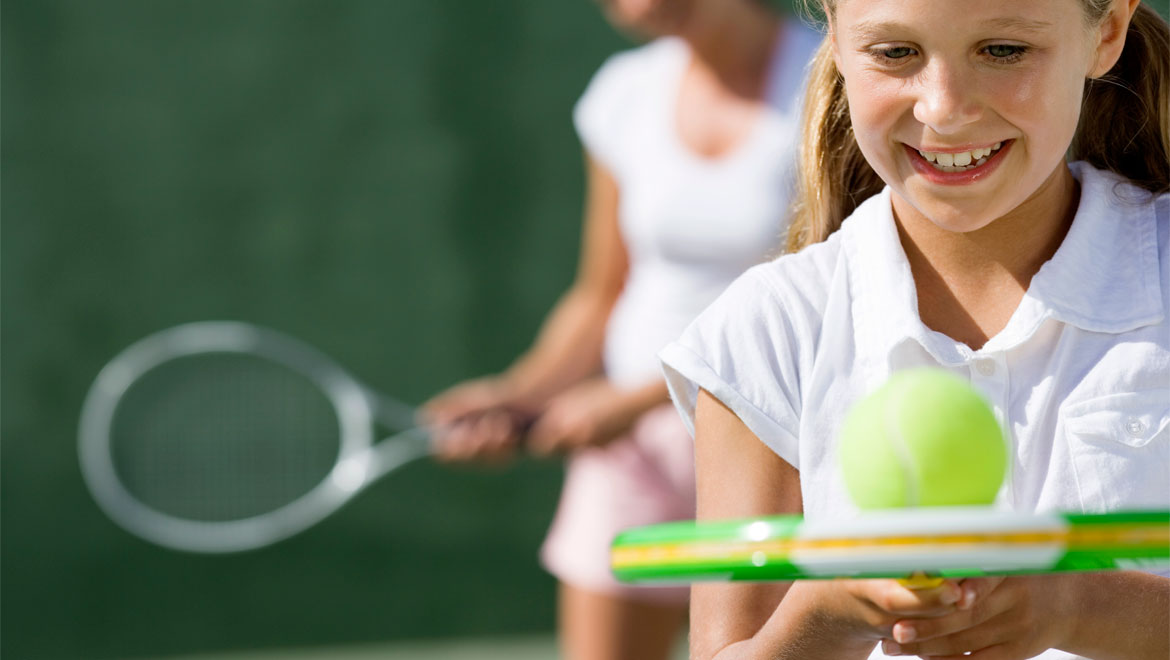 Girl with tennis ball and mother in background