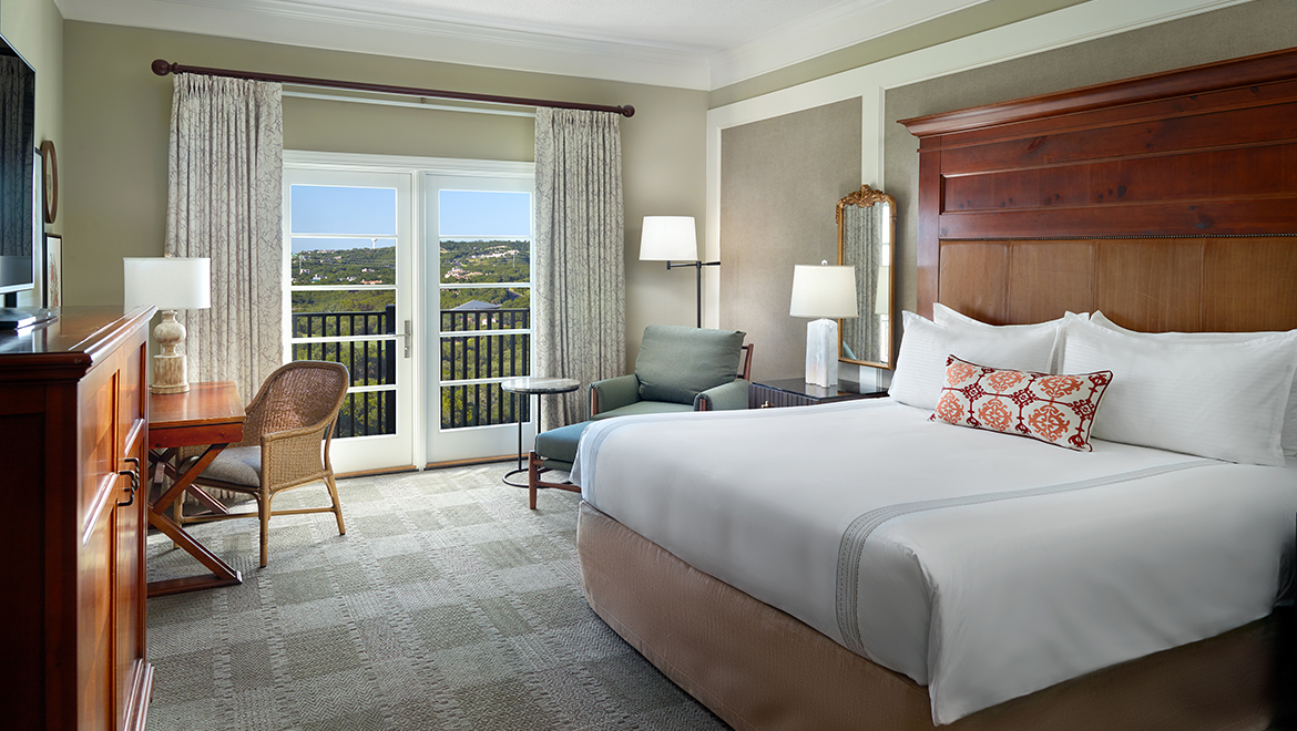A Fairway King Room featuring a juliette-style balcony with French doors, activity desk and lounge chair.